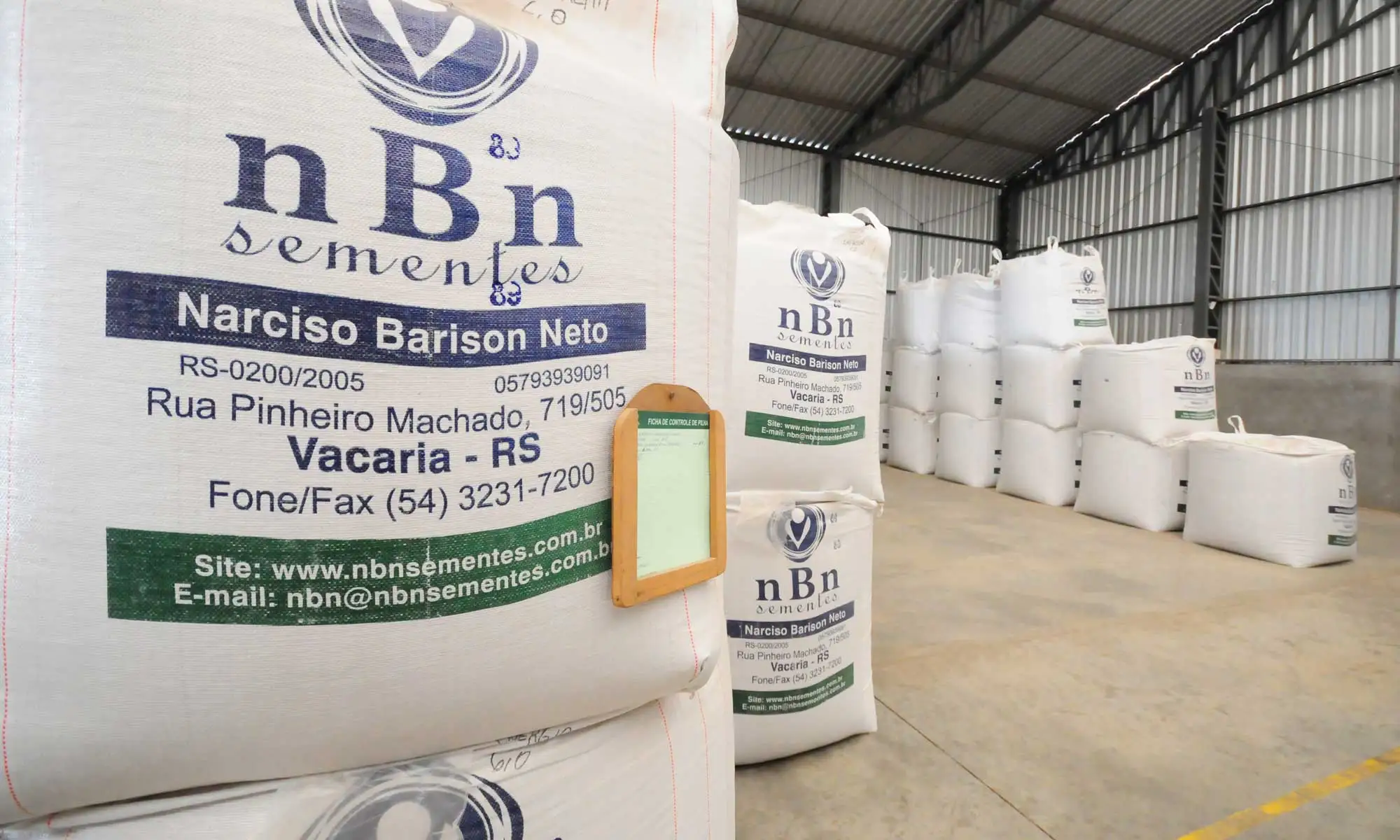Big bags de semente empilhados no armazém, com a marca nBn sementes e o nome Narciso Barison Neto impressos.